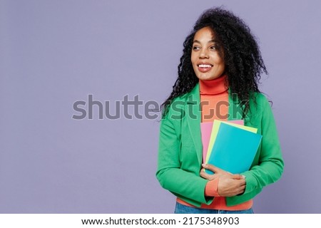 Teacher smiling elegant charismatic fun young black curly woman 20s wears green shirt looking aside holding in hands coloured textbooks isolated on plain pastel light violet background studio portrait