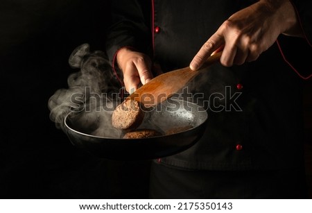 The chef is frying burger cutlets in a frying pan. Close-up of a cook's hands with a hot pan in the kitchen. Free space for advertising.