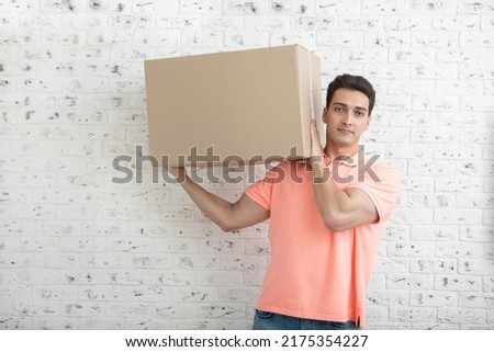 Handsome man carrying heavy box in front of white brick wall background Royalty-Free Stock Photo #2175354227