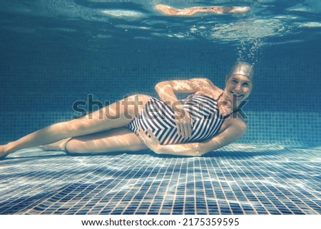 pregnant woman diving in a pool of blue water.  Underwater photo.