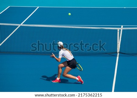 A girl plays tennis on a court with a hard blue surface on a summer sunny day Royalty-Free Stock Photo #2175362215