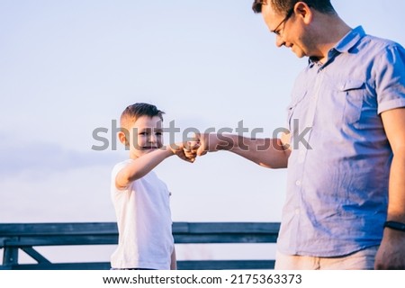 Portrait of american father bumping smiling son. Dad and boy child kid make hand gesture nonverbal sign show mutual support respect in family relations.