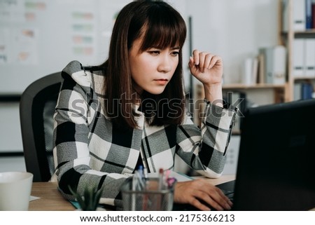 asian woman creative worker having blurred vision is squinting eyes while leaning forward close to the computer monitor trying to see clearly at office desk. Royalty-Free Stock Photo #2175366213