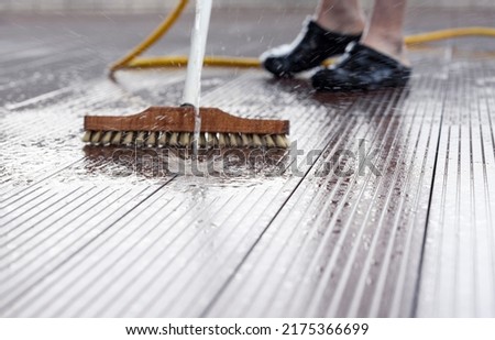 Detail of a man with a scrubbing brush and a water hose making spring cleaning on a wooden terrace