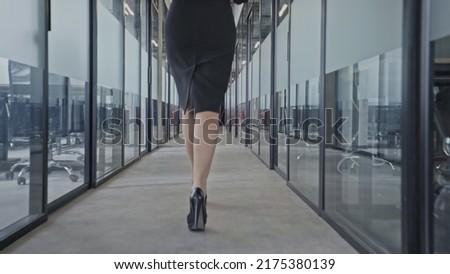 Back view of business woman on high heels walking along corporate building corridor Royalty-Free Stock Photo #2175380139