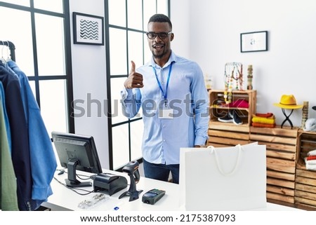 Young african man working as manager at retail boutique doing happy thumbs up gesture with hand. approving expression looking at the camera showing success. 