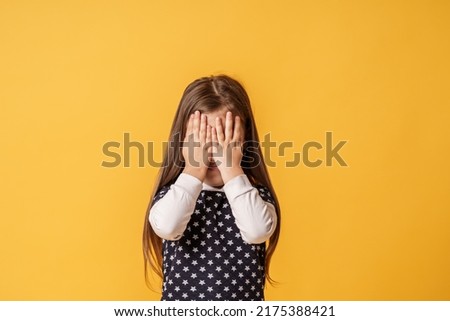 shy child who is ashamed of his bad behavior without showing his tears. a little girl covering her face with her hands is afraid of a horror movie on a yellow background. Body language Royalty-Free Stock Photo #2175388421