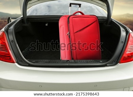 Red suitcase in car trunk and free space for your decoration. Landscape of mountains and road. Sunset time. 