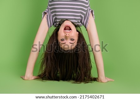 Upside down view portrait of attractive strong cheerful lucky girl standing on hands training isolated over bright green color background Royalty-Free Stock Photo #2175402671