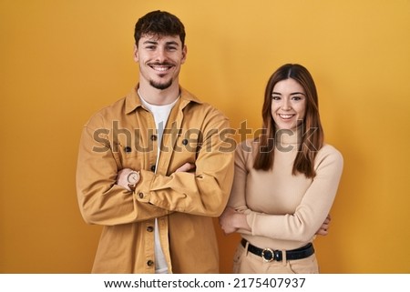 Young hispanic couple standing over yellow background happy face smiling with crossed arms looking at the camera. positive person. 