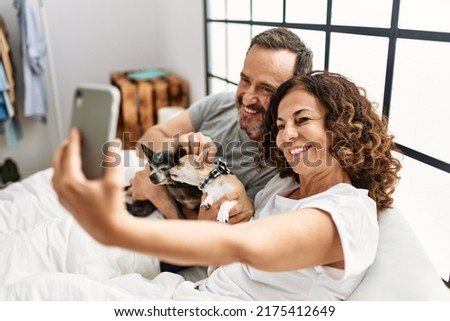 Middle age hispanic couple smiling happy making selfie by the smartphone. Lying on the bed with dogs at home.
