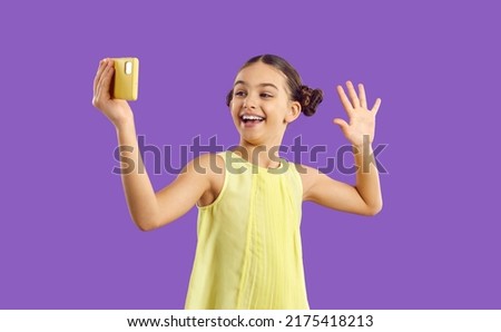 Children and technology. Cheerful trendy kid girl influencer record video vlog and makes selfie on purple background. Funny cute preteen girl having fun waving hand looking at mobile phone camera.