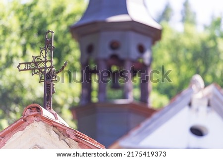 the picture shows a broken cross on top of the roof. Behind the cross in the background is a turret with a small bell. It's a sunny day and the roofs glisten from the reflected rays of light