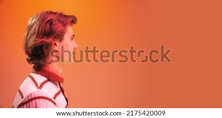 Side view portrait of young handsome man posing, looking away isolated over orange studio background in neon light. Concept of youth, fashion, lifestyle, emotions. Copy space for ad, flyer