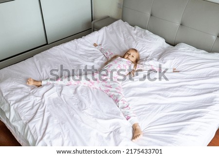 Beautiful little girl in pajamas jumping on the bed with white blanket at home. Stay at home during coronavirus covid-19 lockdown and have a fun. Happy childhood concept
