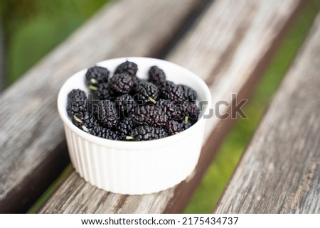Group of mulberries in a white cup on a wooden table.