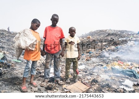 Three miserable African streetboys make their living by recycling metals, plastic and other materials from a dirty and smoking landfill