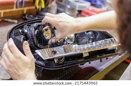 Car headlight in repair close-up. The car mechanic installs the lens in the headlight housing. The concept of a car service.Installation of LED lenses in the headlight. LED lens.Restoration of optics. Royalty-Free Stock Photo #2175443965