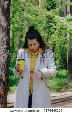 Young girl walking outdoors using her phone taking pictures and drinking a coffee rpounded of beautiful nature backround