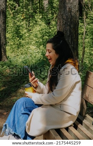 Young girl walking outdoors using her phone taking pictures and drinking a coffee rpounded of beautiful nature backround