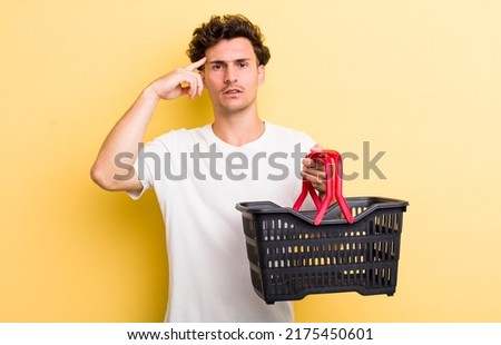 young handsome guy feeling confused and puzzled, showing you are insane. empty shopping basket concept