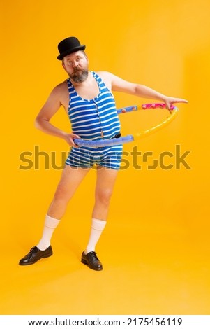 Make the waist. Cute fat young man wearing retro striped swimsuit and vintage bowler hat doing sport exercises isolated on bright yellow background. Vacation, summer, funny meme emotions concept.