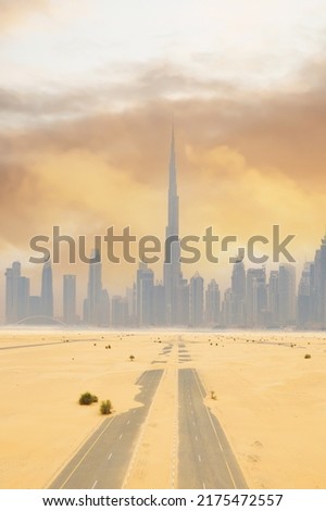 View from above, stunning aerial view of a deserted road covered by sand dunes with the Dubai Skyline in the distance during a beautiful sunset. Royalty-Free Stock Photo #2175472557