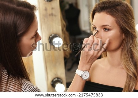 Pofessional make-up artist and her working process during makeup routine for young and beautiful model before photo shoot
