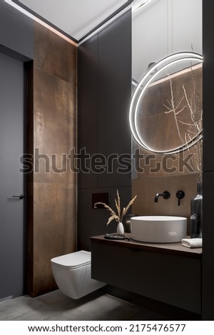 Modern and elegant bathroom with toilet, small washbasin and rusty wall tiles and round, led lamp Royalty-Free Stock Photo #2175476577