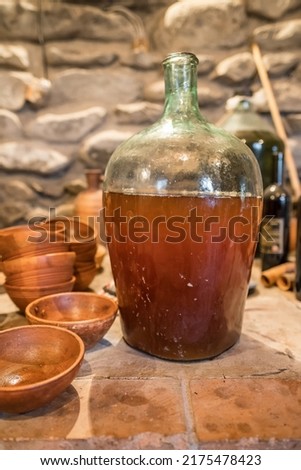 Young wine in big glass bottle next to vintage georgian terracotta jug in authentic Georgian wine cellar. Rural georgian still life concept. Shallow DOF