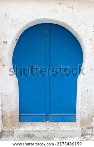 Arched blue front door without patterns in white stone wall in Tunisia. Local architecture details in North Africa