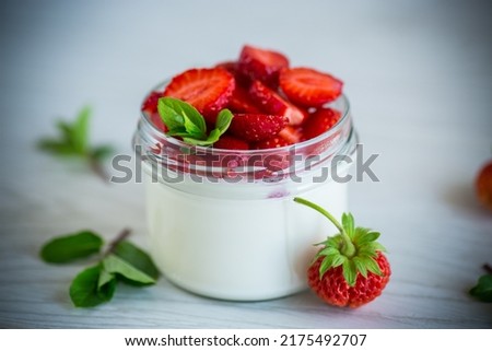 Sweet homemade yogurt with fresh ripe strawberries in a glass jar on a light wooden table