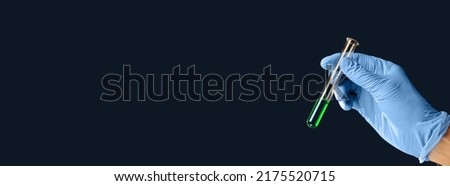 Horizontal shot of hand holding green liquid in test tube close up on dark background. The concept of searching for an antiviral drug. Royalty-Free Stock Photo #2175520715