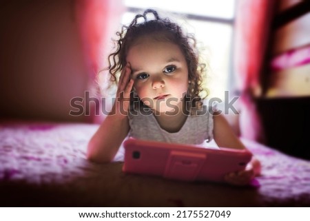 A little girl playing tablet lay on the bedroom