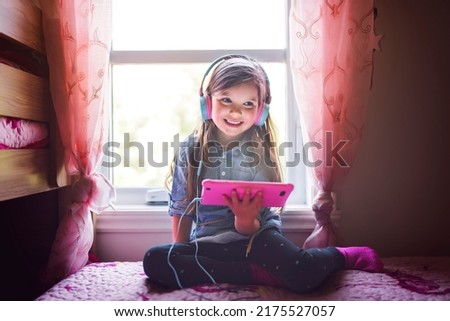A little girl playing tablet lay on the bedroom with headphone on ear