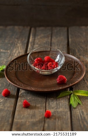 raspberries in a transparent saucer on a ceramic plate on wooden boards. Fruits, food, summer