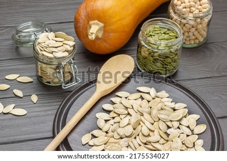 Pumpkin seeds in glass jars. Wooden spoon and seeds on board. Top view. Dark wooden background