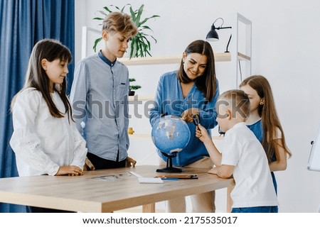 Teacher and children in class are looking at globe, teacher helps explain the lesson to the children in the class at a desk. Educational school process, bright room and interesting learning Royalty-Free Stock Photo #2175535017