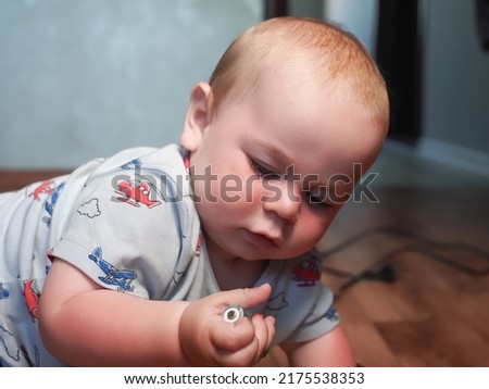 A little baby is holding a dangerous battery in his hands. The boy takes a life threatening small object in his mouth Royalty-Free Stock Photo #2175538353