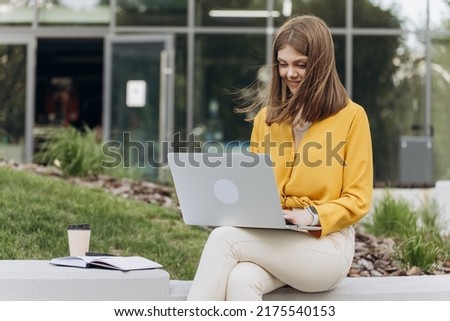 Young woman is sitting on a bench of city park and using laptop computer. Focused european business woman student entrepreneur typing on pc study online course with laptop. Concept of freelance