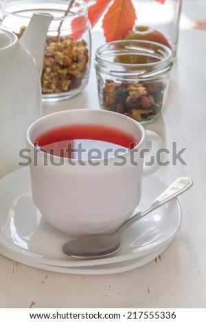 Breakfast - hibiscus tea, granola, apple, colored leafs on white wood background