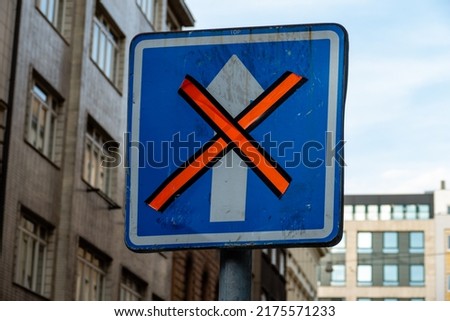 One way street road sign temporally invalidated with orange tape. White arrow in blue background, crossed out. Urban background.  Royalty-Free Stock Photo #2175571233