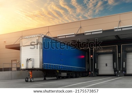 Innovative modern logistics warehouse center complex building exterior bay gate semi-trailer unloading goods distribuition warm blue sunset sky background. Cargo storage facility industry building Royalty-Free Stock Photo #2175573857