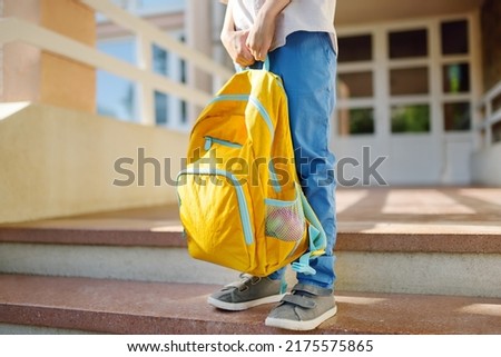 Little student with a backpack on the steps of the stairs of school building. Close-up of child legs, hands and schoolbag of boy standing on staircase of schoolhouse. Kids back to school concept. Royalty-Free Stock Photo #2175575865