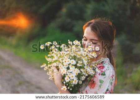 Portrait woman with chamomile flowers at sunset. Life without allergies, breathe freely. Woman having fun in summer on nature. Woman dreaming and smiling against the background of a camomile field.