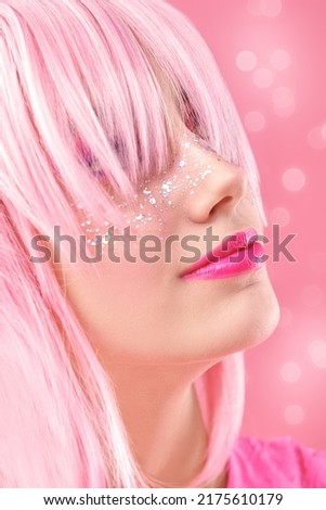 Asian style, anime. Portrait of a pretty teen girl with pink makeup and glitter freckles posing in pink wig on a pink background with shining lights. 