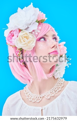 Beauty girl. Portrait of a beautiful girl with bright pink makeup and pink hair with floral wreath on her head. Japanese anime style. Spring and summer beauty. Blue background.