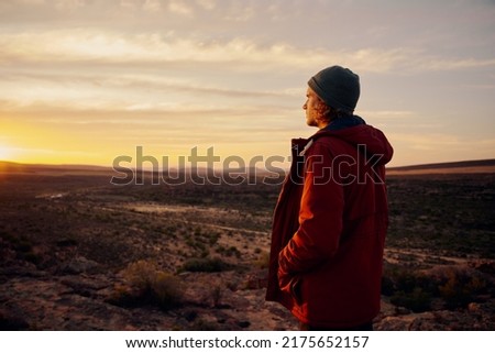 Thoughtful man wearing jacket and cap standing on mountain looking at morning sunrise Royalty-Free Stock Photo #2175652157