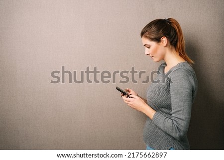 Young woman looking at her cell phone, brown wall with copy space