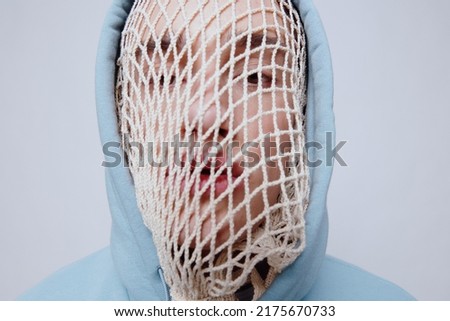 a man suffering from problems with a mesh on his face is standing in a light blue hoodie on a light background facing the camera. close-up photography in the studio